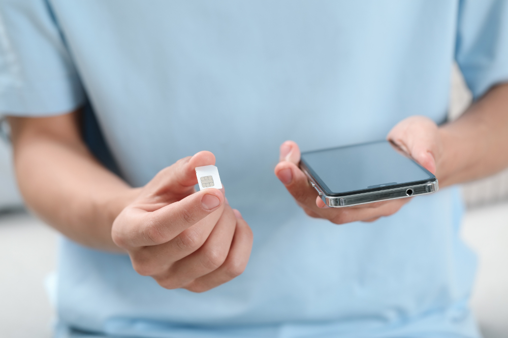 A man holding a SIM card and a smartphone indoors