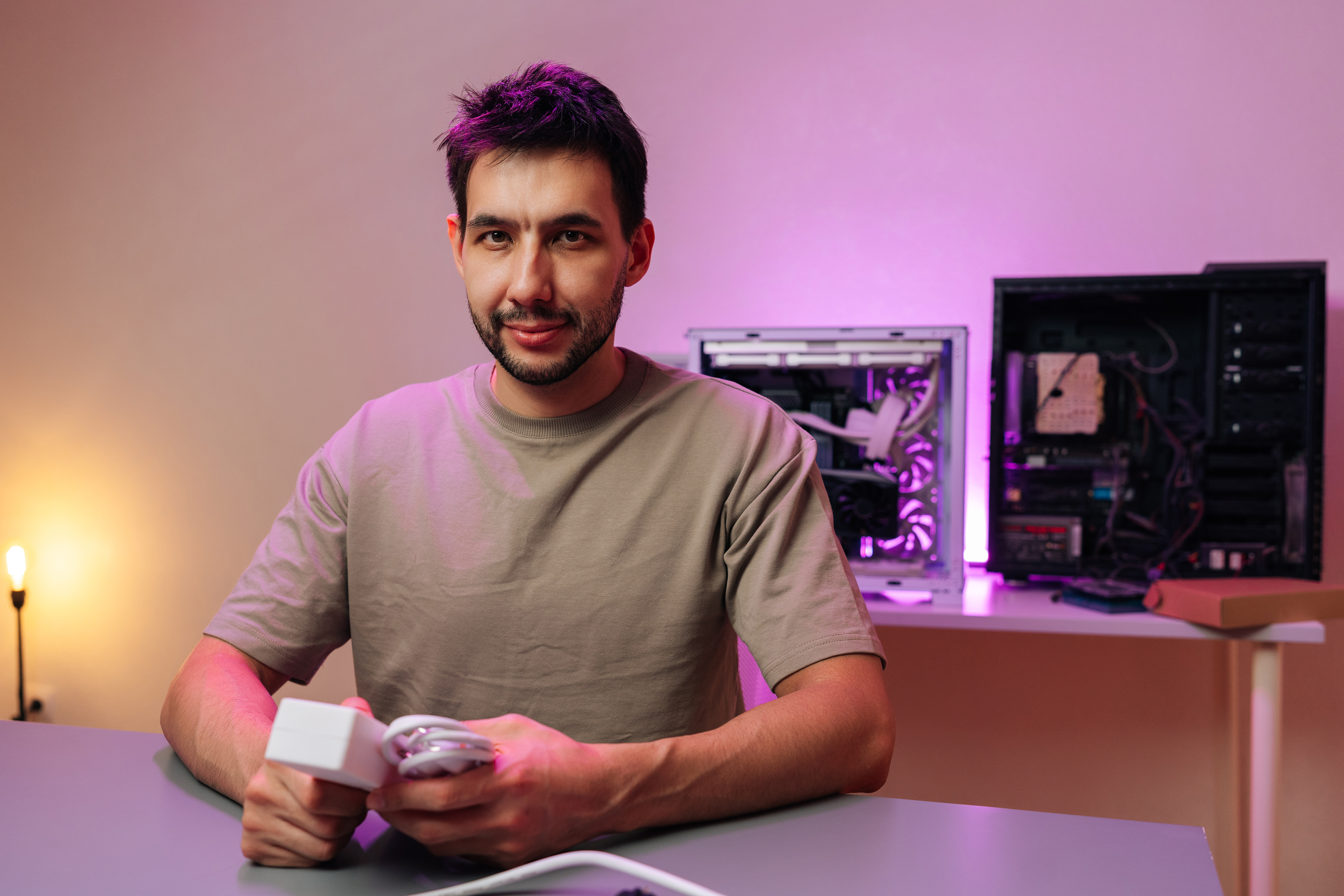 Man smiling at desk with open PC cases and purple RGB lighting in background