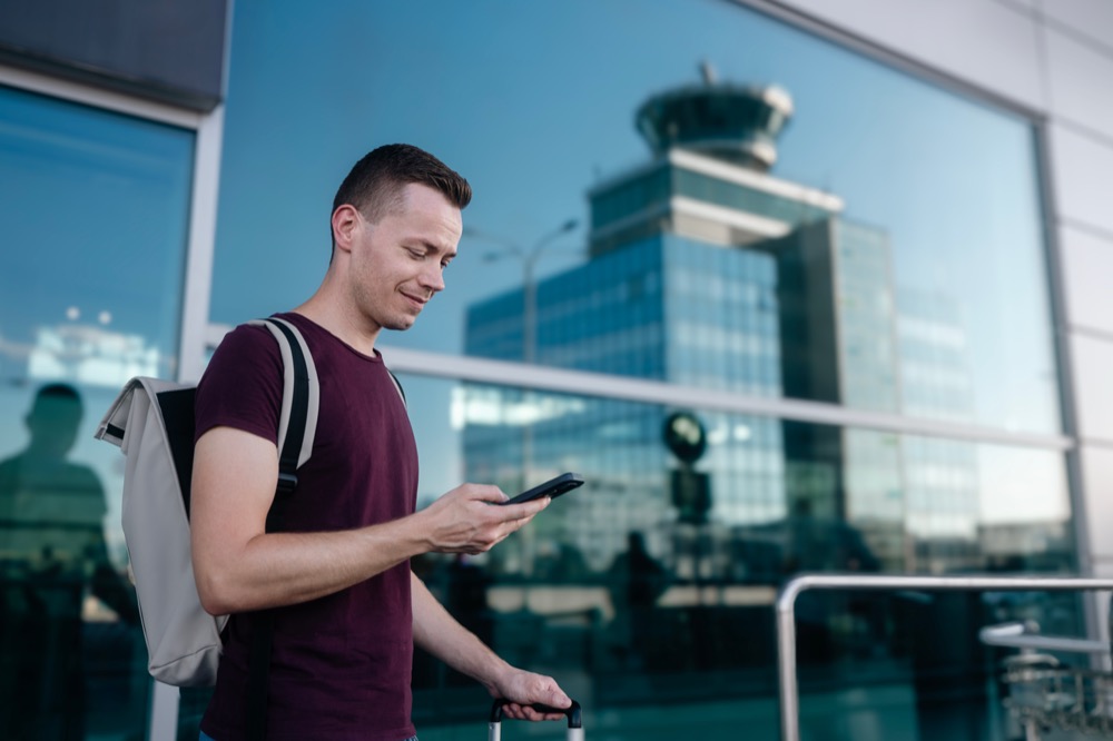 Traveler with a backpack using his phone at an airport terminal