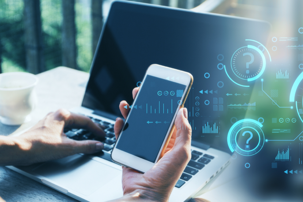 Hands using laptop and smartphone with floating digital question marks