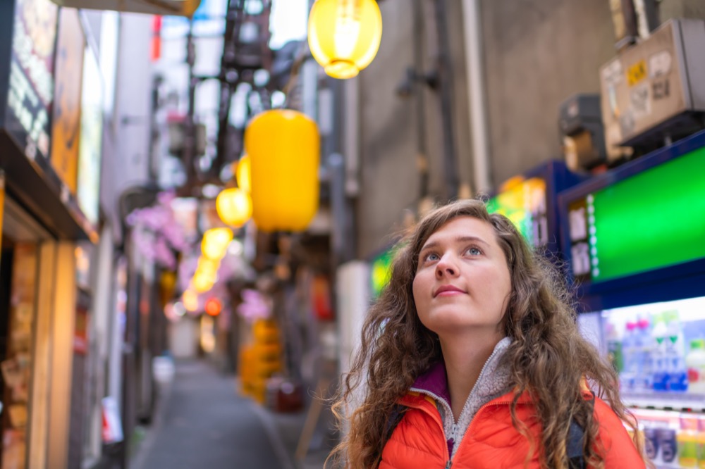 A young woman looking up in a narrow alley decorated with yellow lanterns